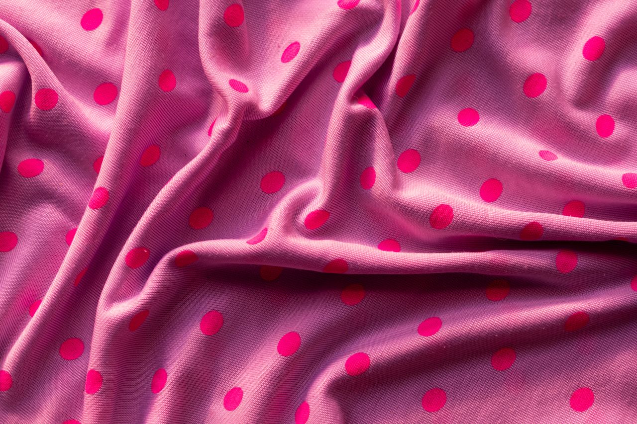 Close-up of vibrant pink fabric with red polka dots, showcasing texture and color.